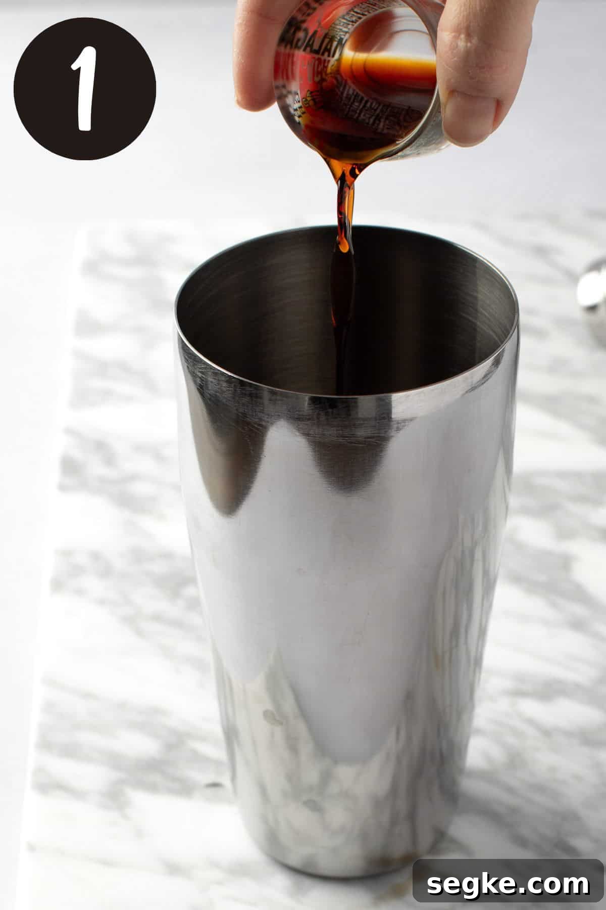 Pouring the kahlua from a shot glass into the cocktail shaker.