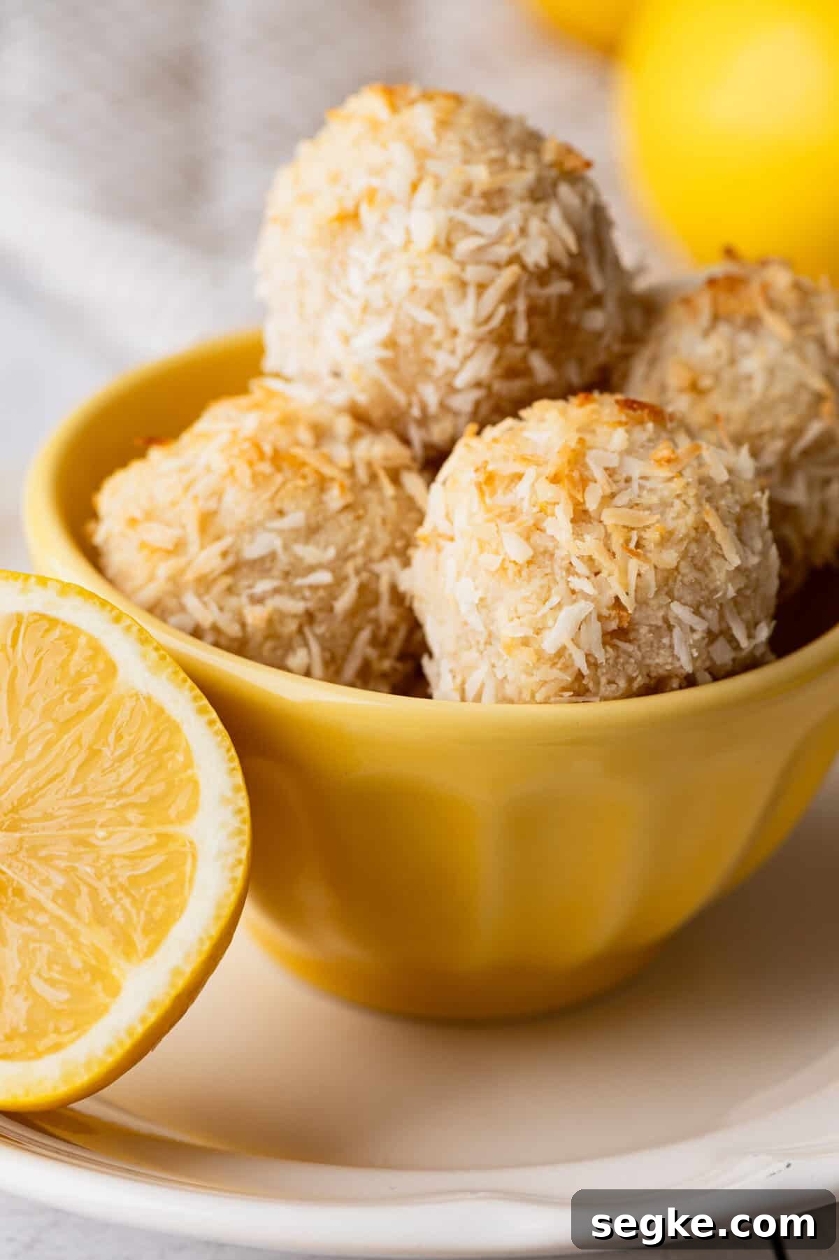 A bowl filled with toasted lemon macaroons with a lemon wedge next to it.