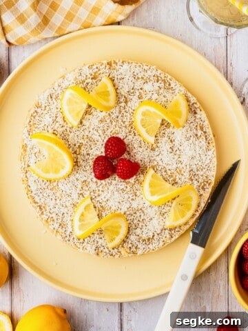 A vegan lemon cheesecake topped with shredded coconut and raspberries.