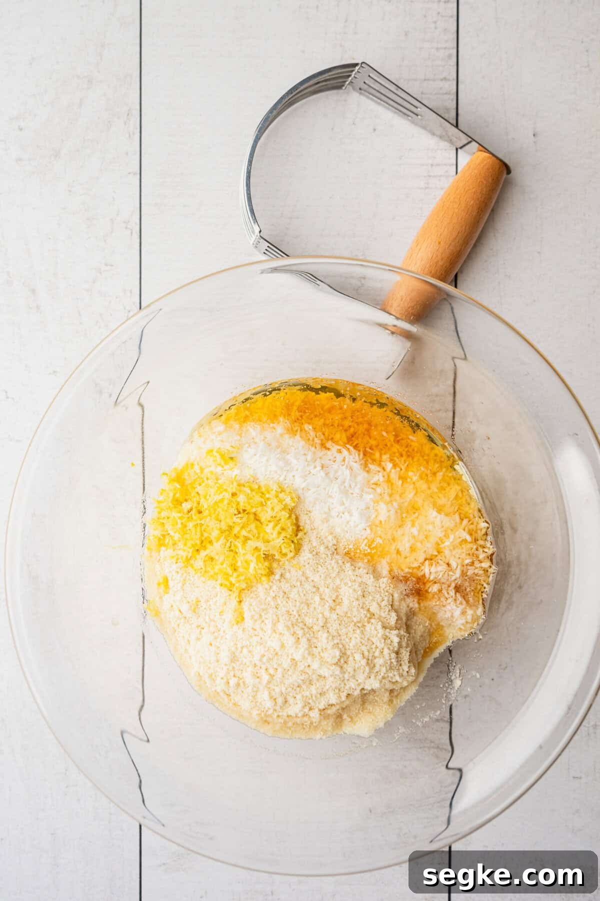 A glass bowl with lemon zest, almond flour, shredded coconut and honey in it.