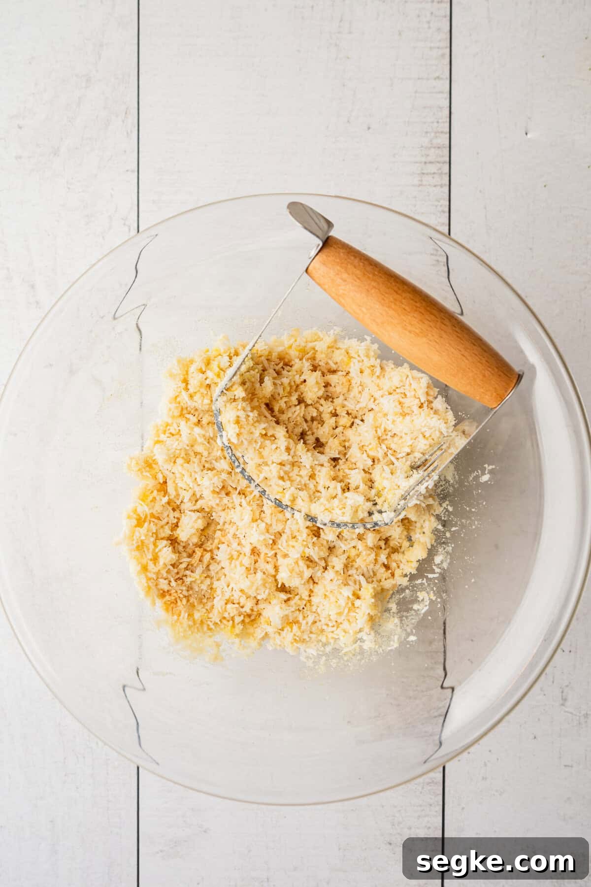 A glass bowl with a crumbly dough in it with a pastry blender in the dough.