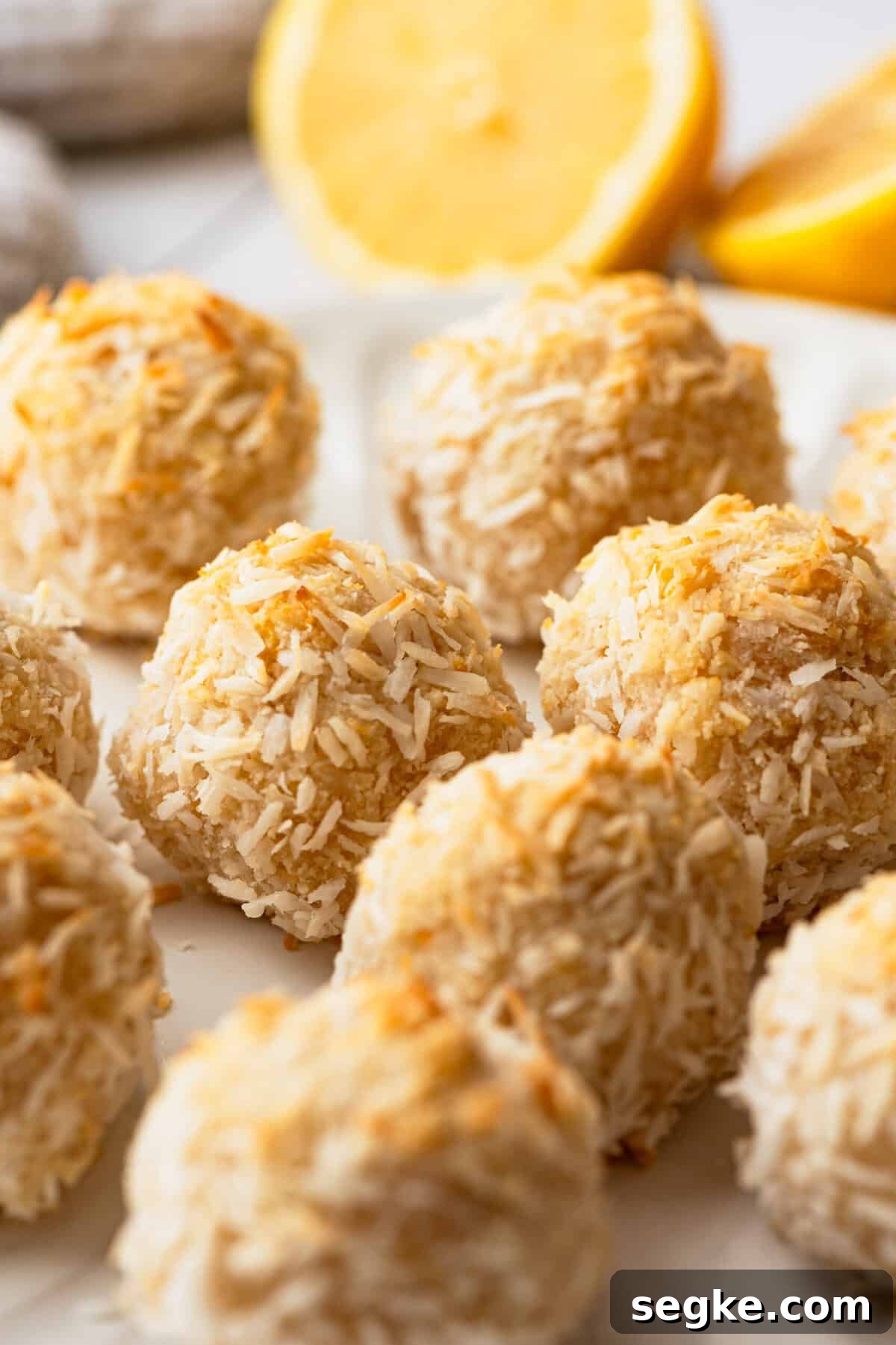 A batch of lemon coconut macaroons on a plate with lemon wedges next to them.