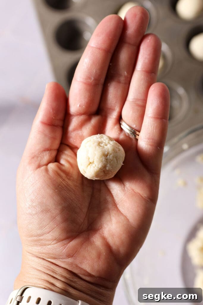 a ball of pie dough in the palm of a hand above a mini muffin tin
