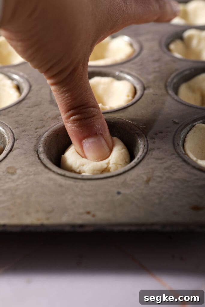 a thumb presses a ball of dough into the basin of a mini muffin tin