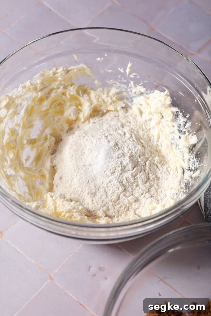 flour and salt sit on top of creamed cream cheese and butter in a bowl on a purple surface