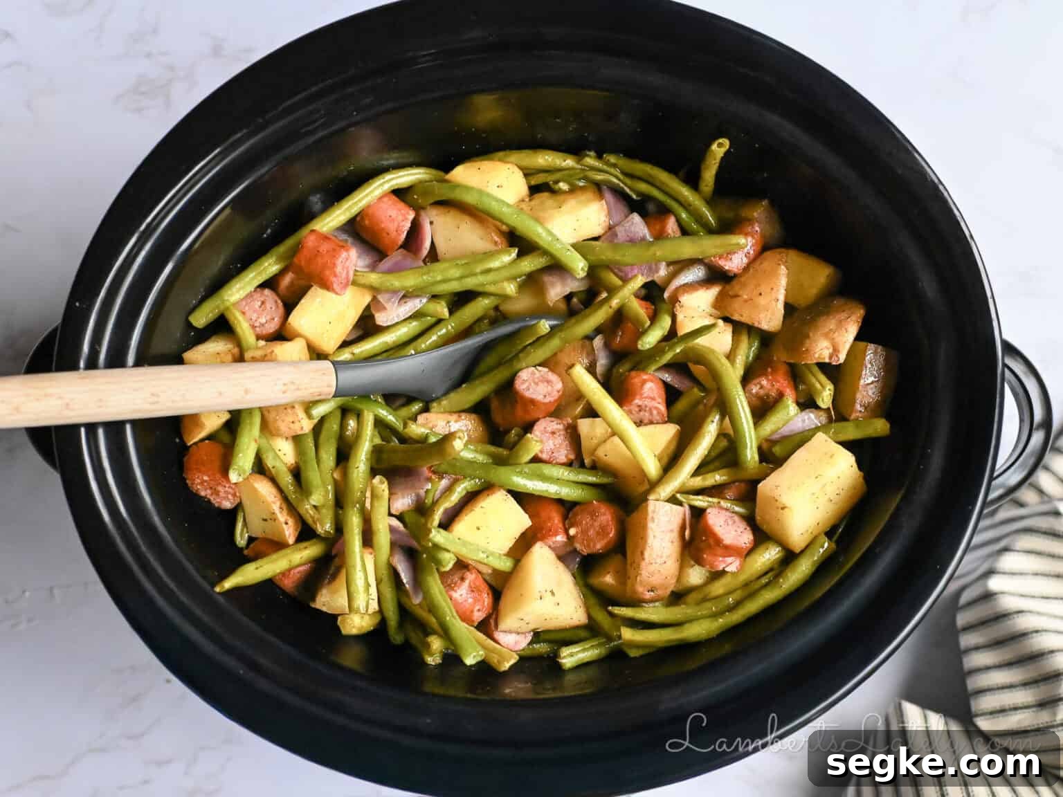 Slow Cooker Southern Swamp Potatoes Recipe 2 crock pot full of swamp potatoes with green beans, sausage, and red onion.