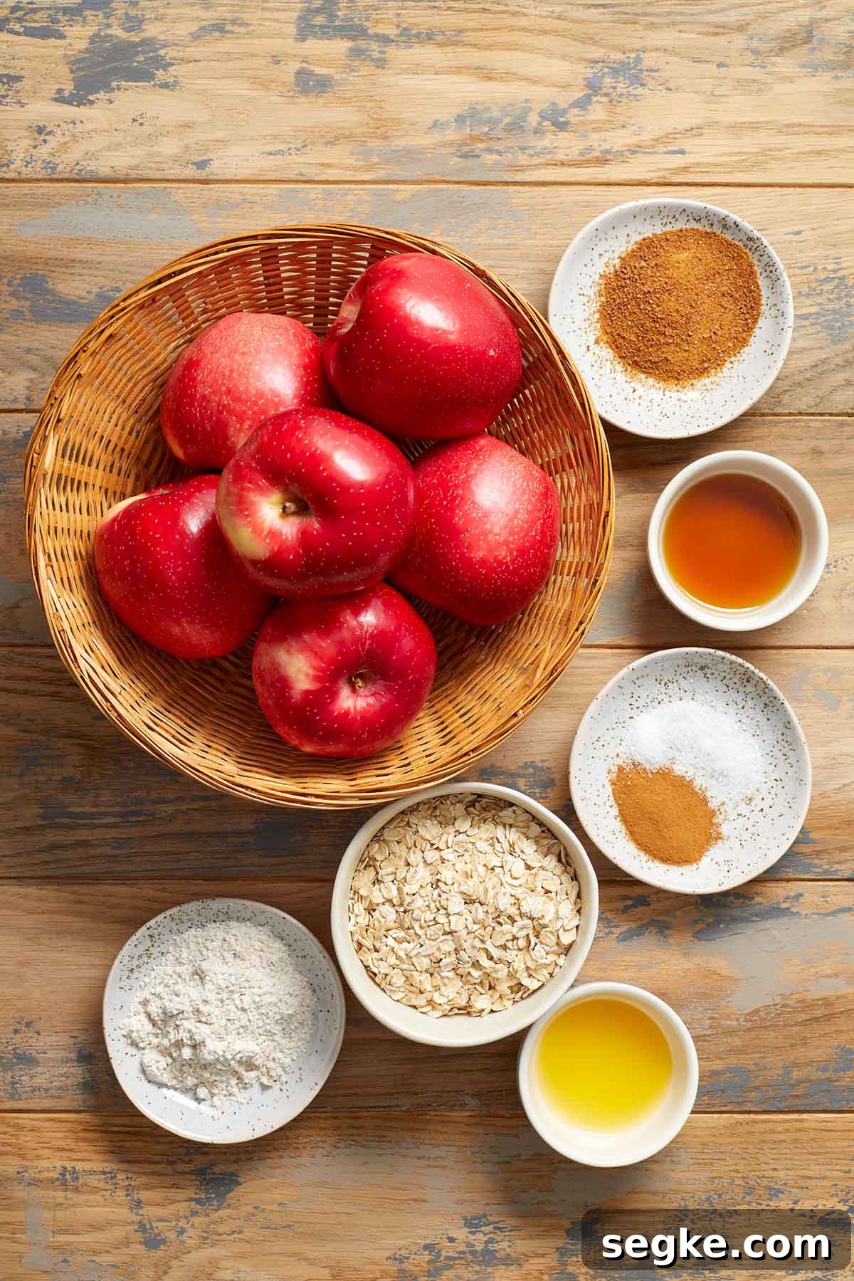 Ingredients to make air fryer apples arranged individually on a wooden surface.