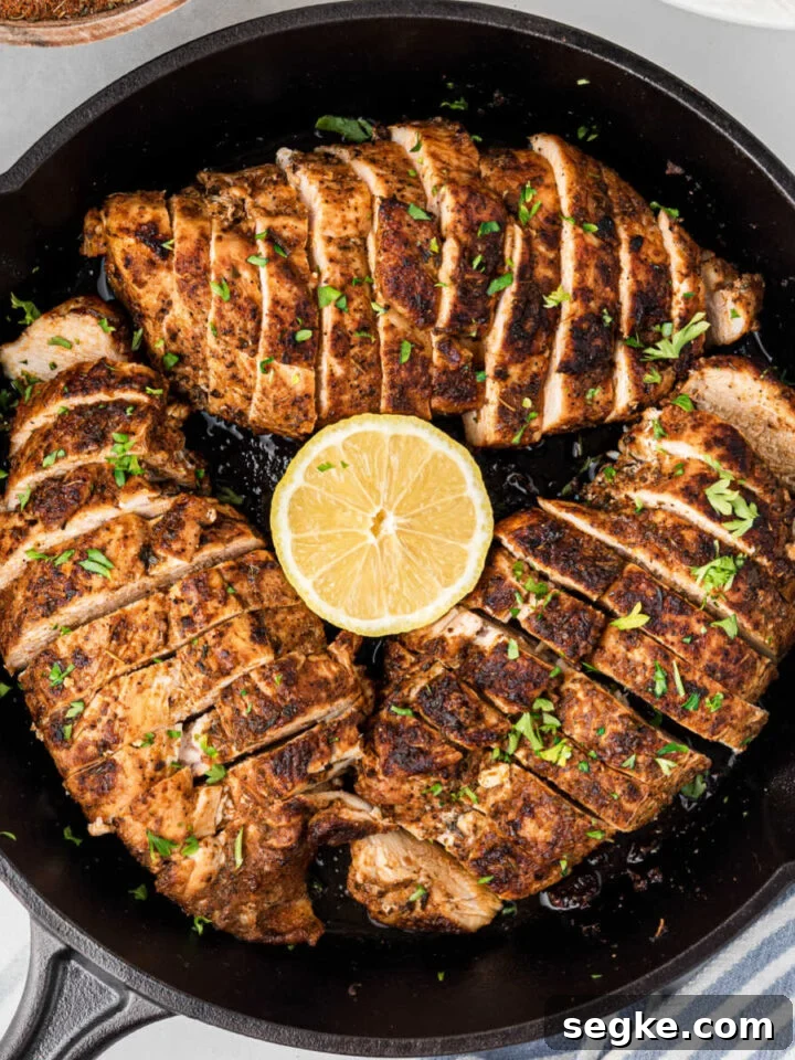 Overhead of a black skillet with three blackened chicken breasts, sliced into even pieces.