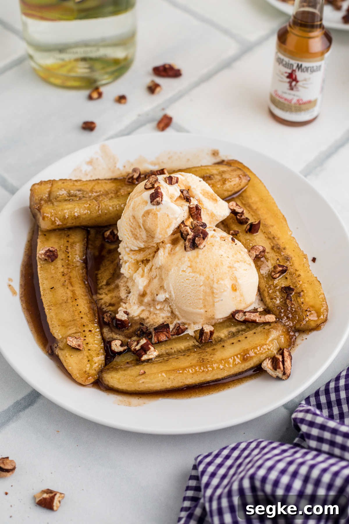Classic New Orleans Bananas Foster Recipe 10 Side shot of a plate of bananas foster with ice cream and pecans with a liquor bottle in the background.