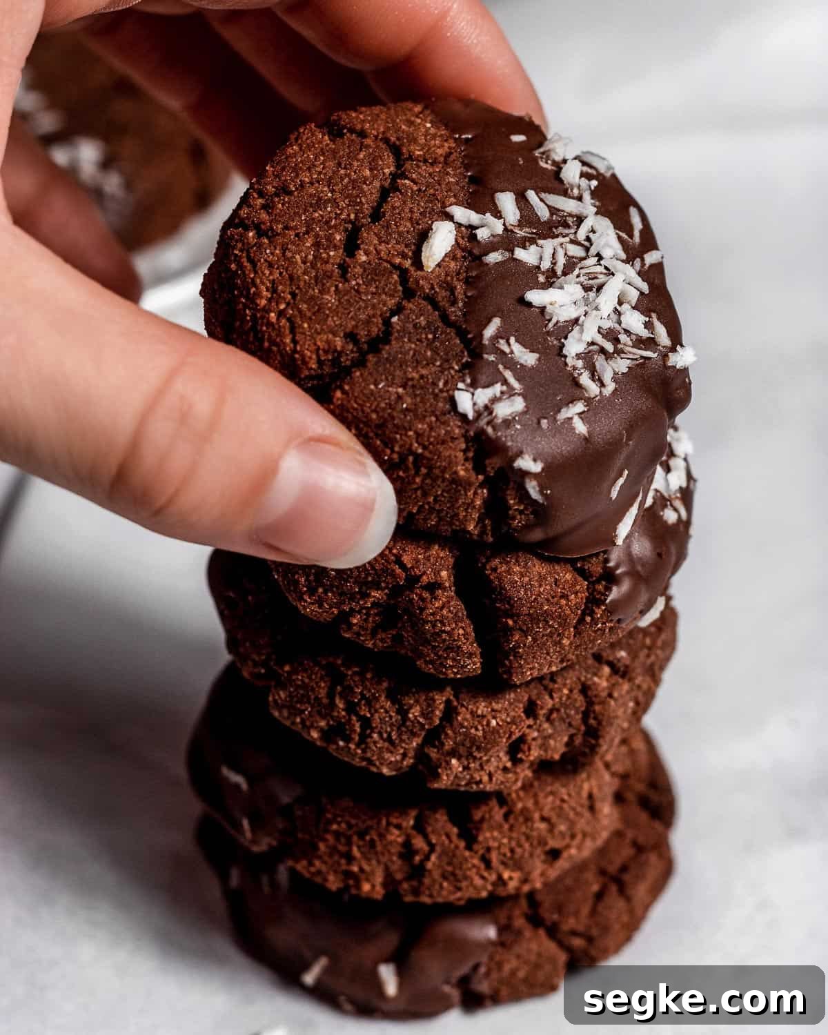Gluten-Free Chocolate Coconut Biscuits Recipe 6 Five chocolate coconut biscuits stacked on top of each other, a hand is holding the top one.