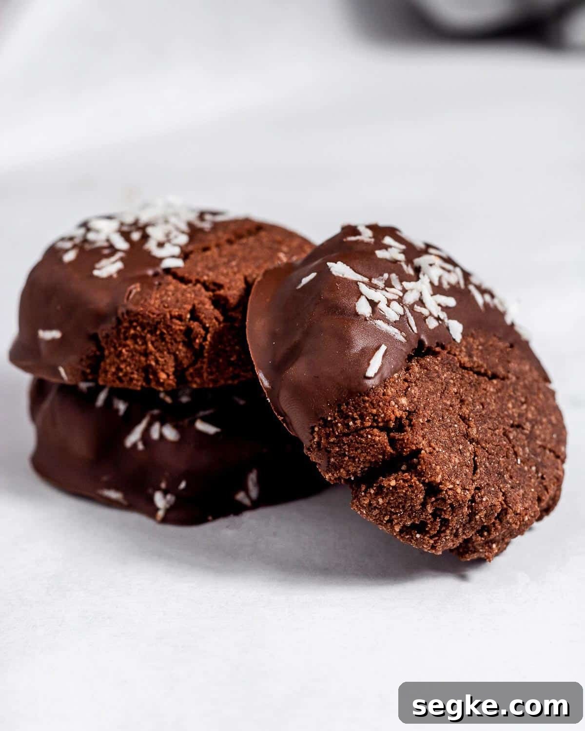 Gluten-Free Chocolate Coconut Biscuits Recipe 7 Two chocolate coconut biscuits on top of each other and a third biscuit is angled up against them.