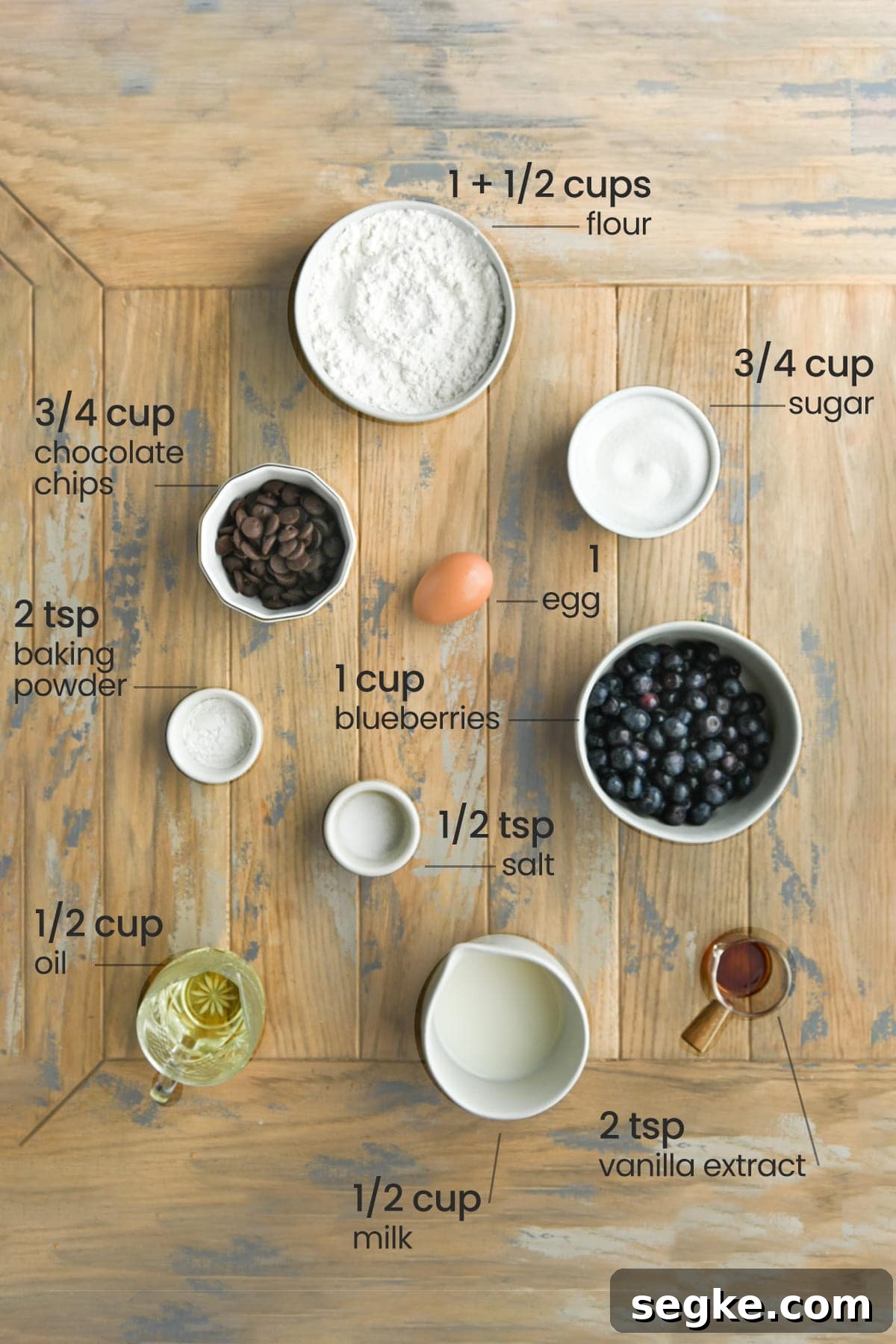 ingredients for blueberry chocolate chip muffins - flour, chocolate chips. sugar, egg, salt, baking powder, blueberries, oil, milk, and vanilla extract
