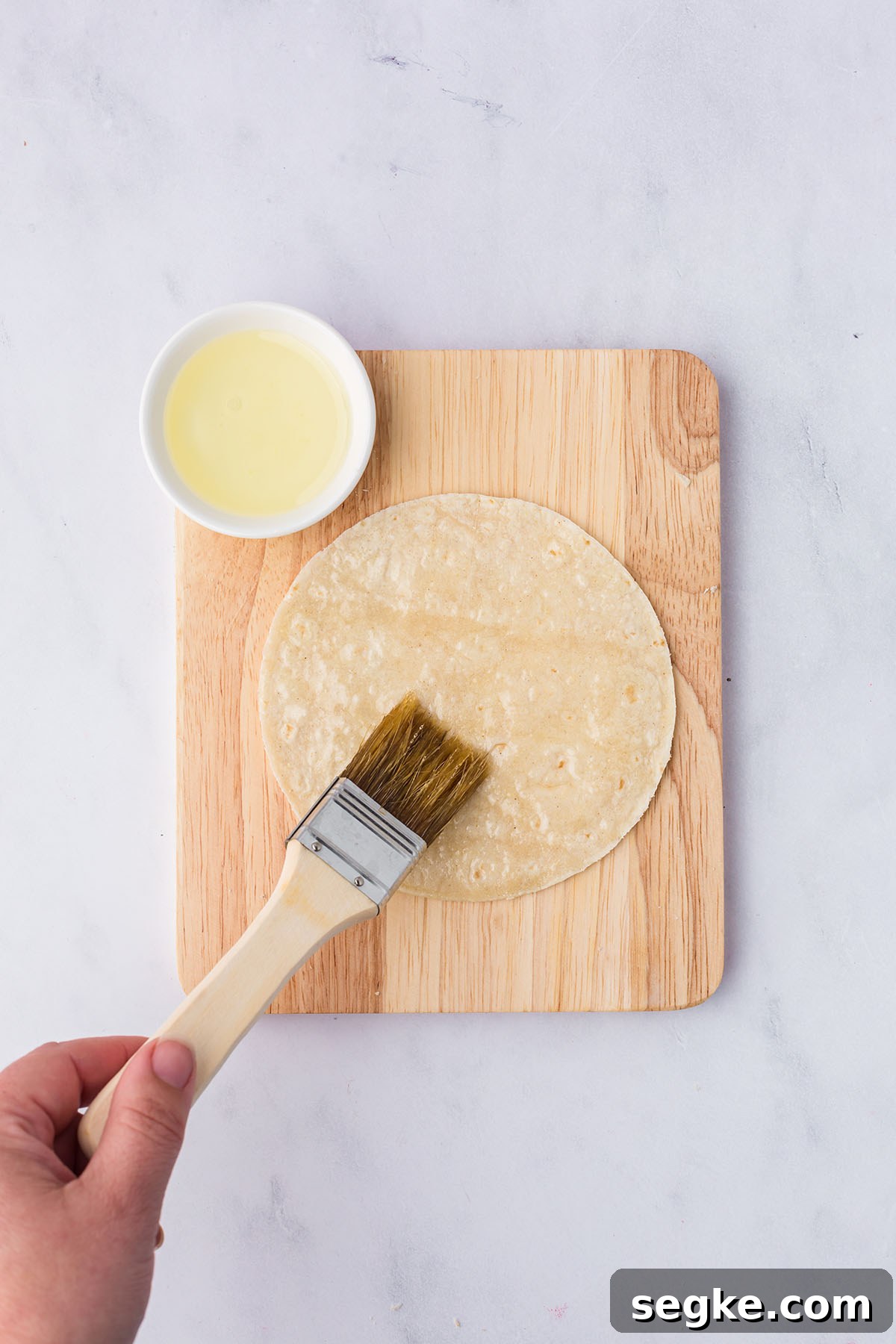 Tortillas are brushed with oil on a wooden cutting board.