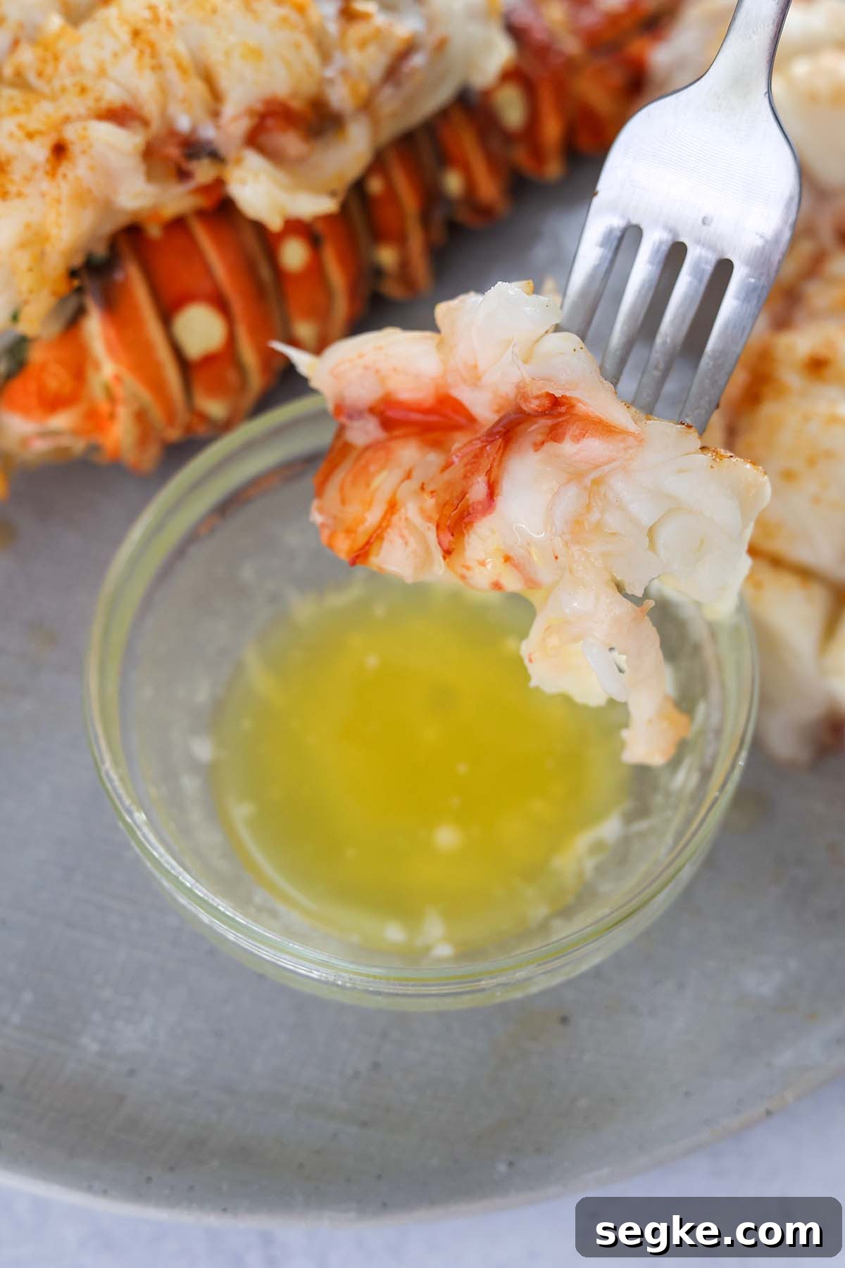 A fork dipping cooked lobster meat into melted butter.