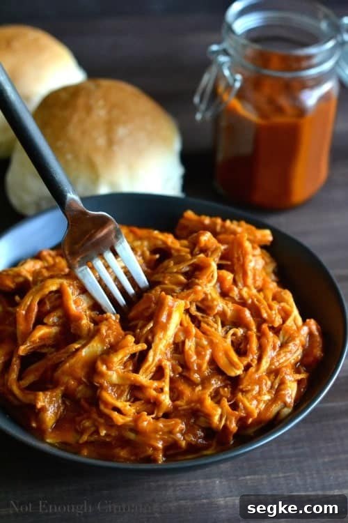 Healthy Peach BBQ Pulled Chicken served in a black bowl with some burger buns an a jar of homemade peach bbq sauce in the background