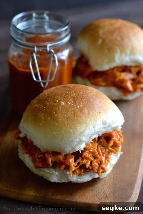 two burger buns loaded with Healthy Peach BBQ Pulled Chicken on a wooden chopping board
