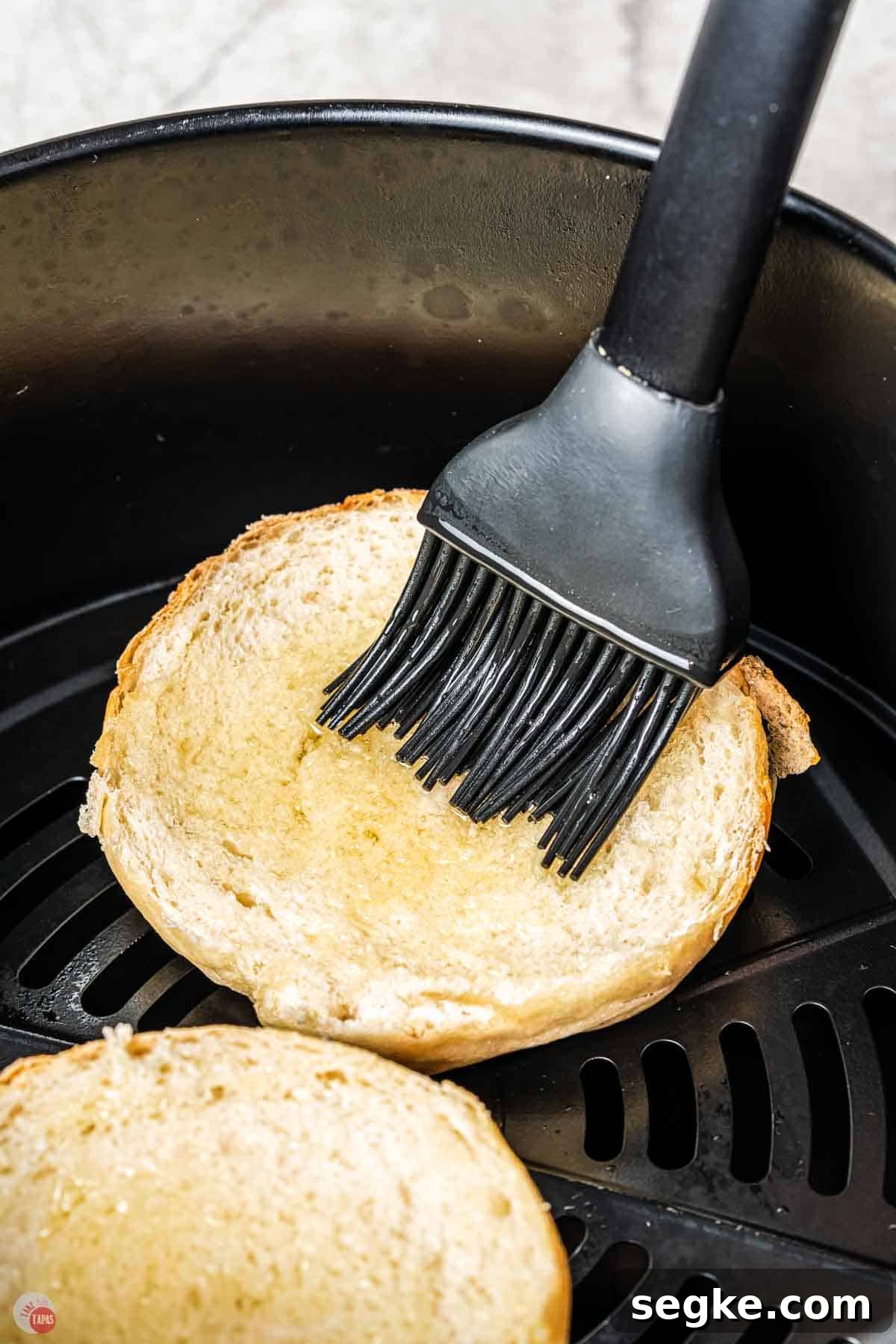 Crispy Air Fryer Pizza Bagels Recipe 4 sliced bagel in an air fryer basket with a silicone brush applying olive oil