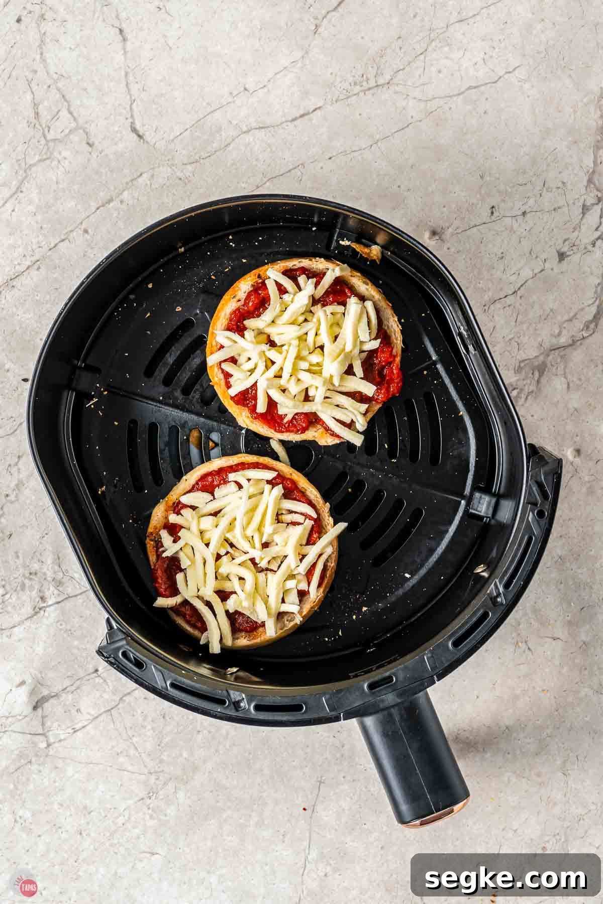 Crispy Air Fryer Pizza Bagels Recipe 6 bagels in an air fryer basket topped with sauce and cheese