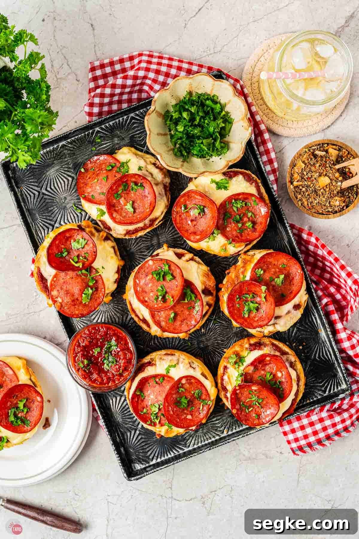 Crispy Air Fryer Pizza Bagels Recipe 9 air fryer bagels on a black tray with small bowls of parsley and spices