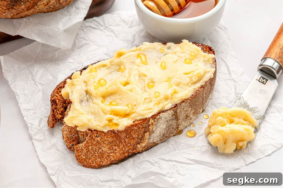 Whipped Honey Butter Recipe in 5 Minutes 5 White paper surface with toasted piece of bread with honey butter. Knife and bowl.