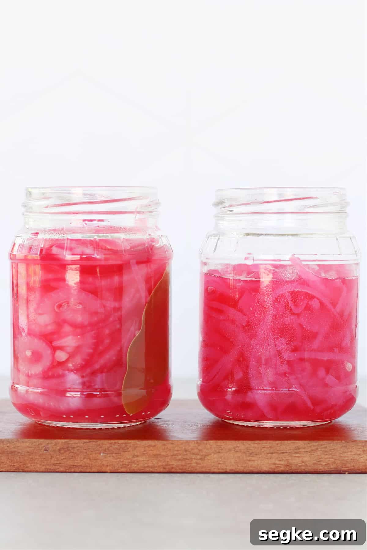 Two jars of pickled red onions on a wooden board.