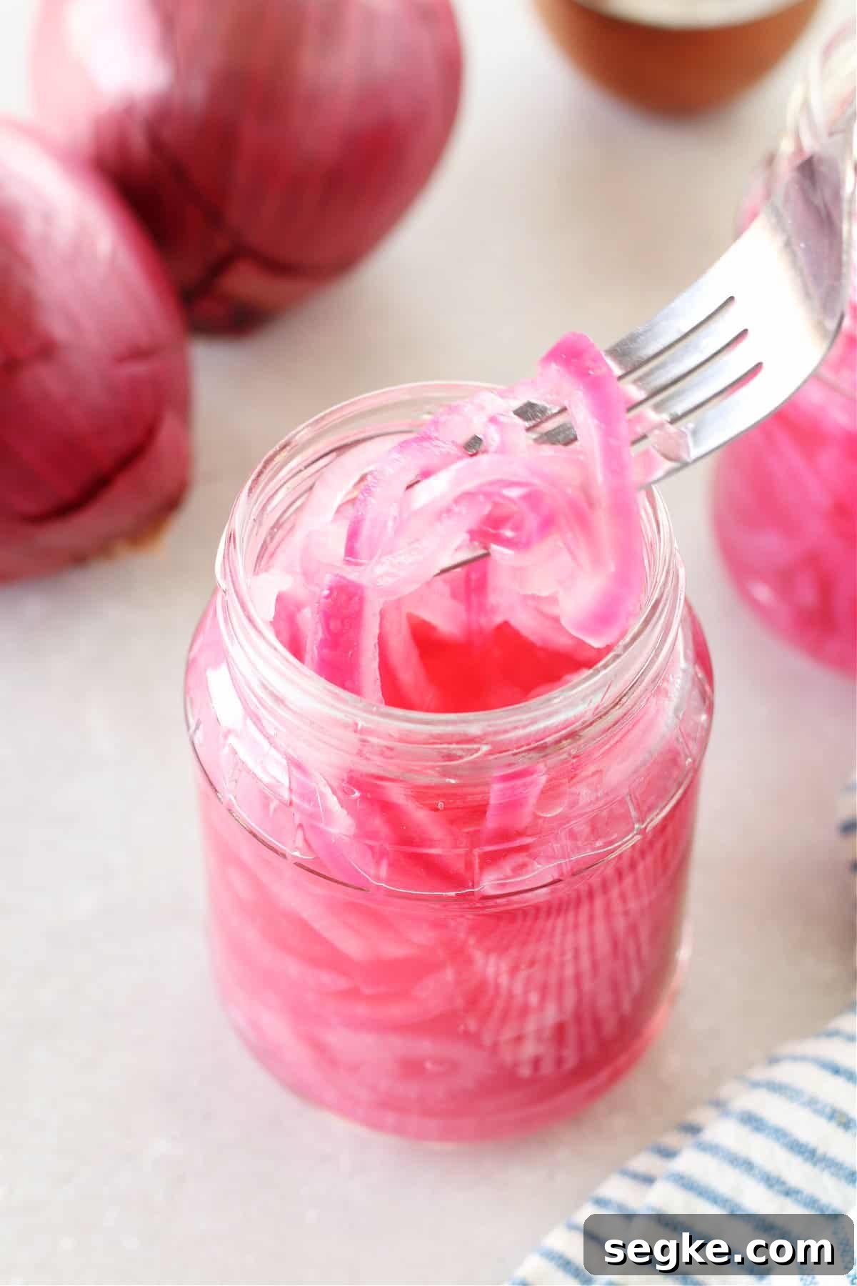 Pickled red onions in a jar and lifted on a fork.