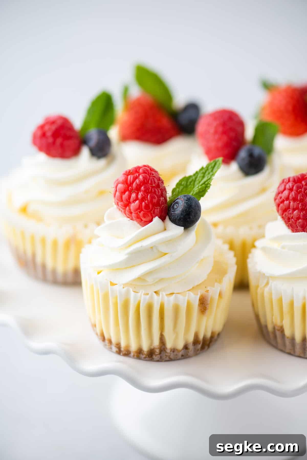 No-Bake Mini Cheesecake Bites Recipe 3 Cheesecake cupcakes on white scalloped-edged cake stand
