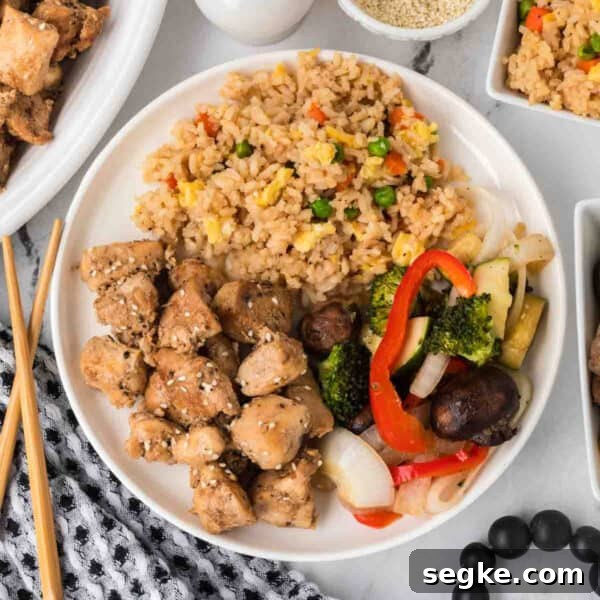 A plate of Hibachi Chicken with sesame seeds, fried rice and vegetables.