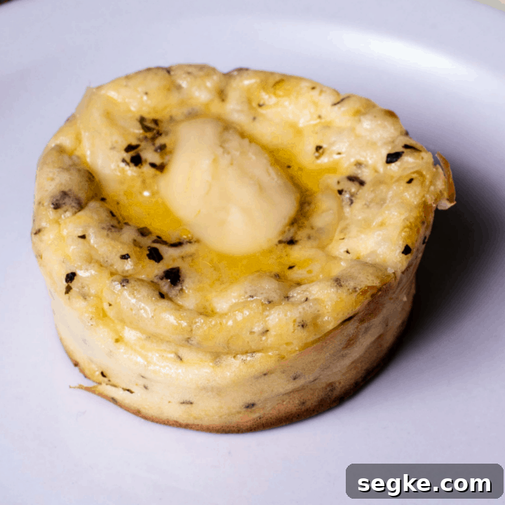 single cream cheese muffin with pat of butter on white plate
